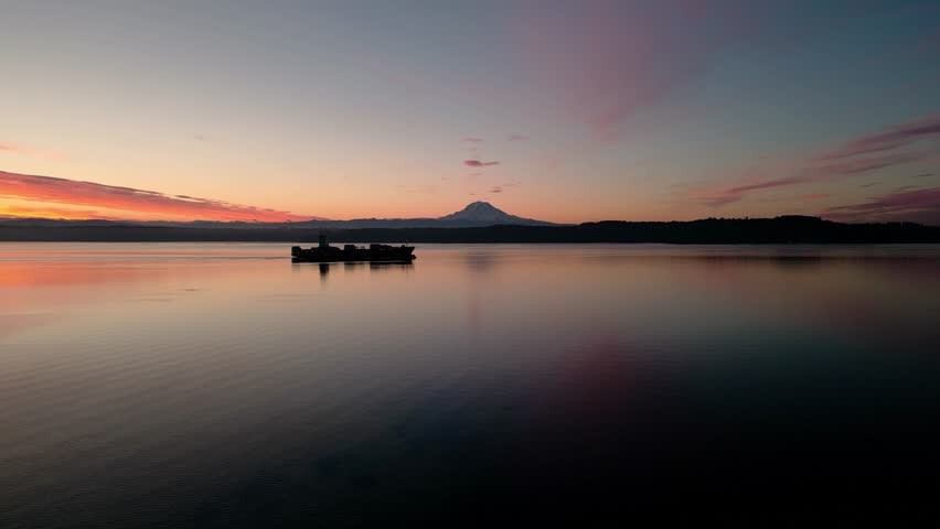 Aerial view cargo ship on Puget Sound. Mount Rainier wallpaper background sunrise or sunset. Peaceful calm background water with boat mountain. pink yellow orange clouds water ripple. 4k 