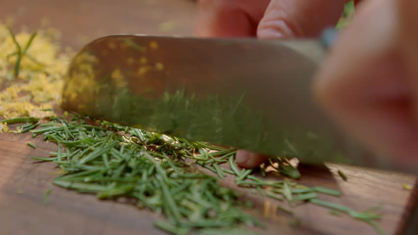Chef Chopping Fresh Herbs on Wooden Board with Large Knife