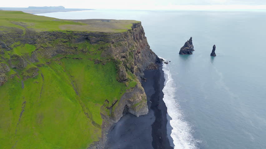 Incredible view of long row of highlands covered with green moss standing majestically by the restless sea with sea stacks on the shore with black sand. High quality 4k footage