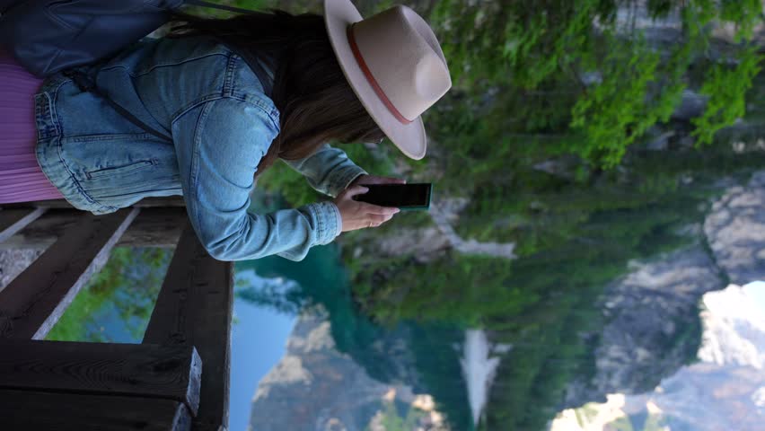 Woman capturing photographs with a smartphone at Lago di Braies, Dolomites, Italy. Vertical