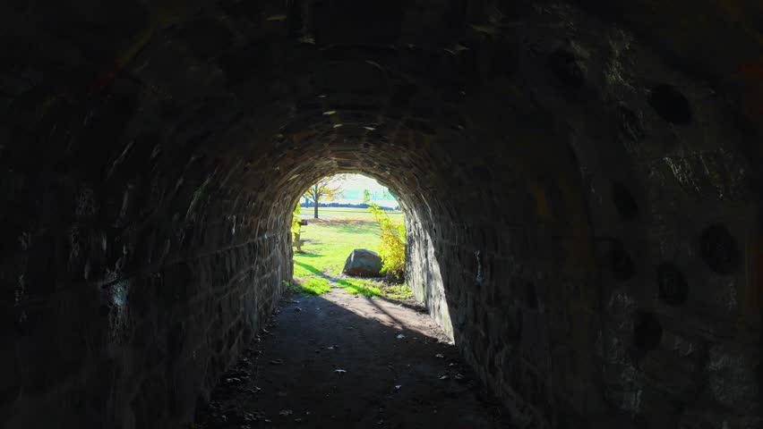 A walk through an old stone tunnel on a sunny day in a park in New Jersey. The camera dolly in through the dark tunnel to reveal the George Washington Bridge in the distance and an empty park.