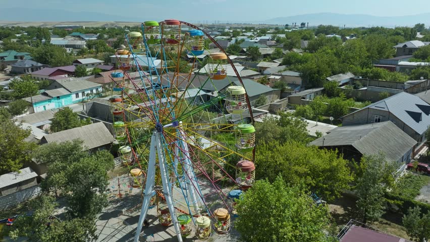 Colorful Ferris Wheel With Rust At Deserted Theme Park In Sayram Near Shymkent In Kazakhstan. aerial orbiting shot
