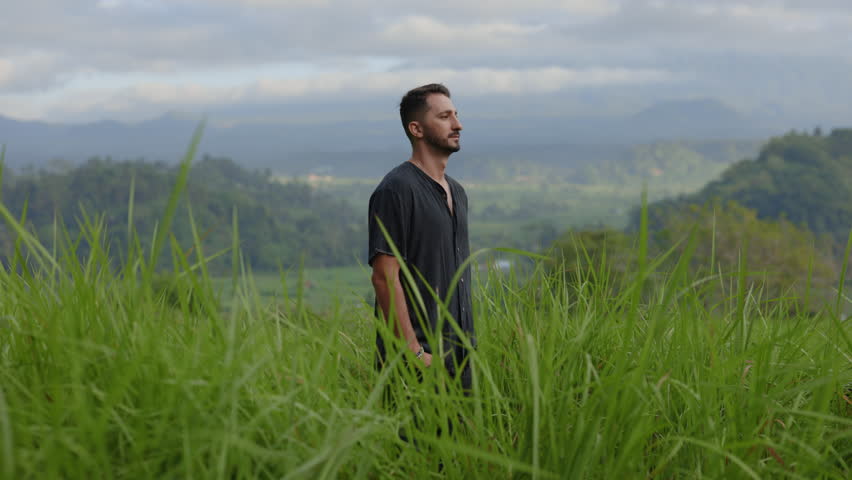 Smiling Multiracial Guy Standing in the Grass Field, Feeling Good. Retreat. Self-Knowledge. Man Outside Posing on the Mountains Background. Male Portrait. Tourism and Traveling Concept | Shutterstock HD Video #1111559689