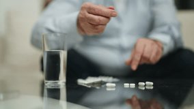 Hands senior man take pills drink water. Sits on couch in living room at home. Sick old male has heath problems, accepting medical therapy taking care about health. Cure preventive treatment concept. - Powered by Shutterstock - Get 15% off with code: PIKWIZARD15
