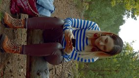 A woman using smartphone in the forest outdoor, smiling. FOMO (Fear of missing out) concept. Vertical video.