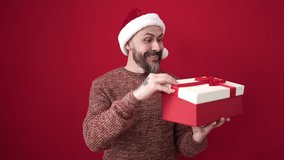 Young bald man wearing christmas hat holding gift looking upset over isolated red background - Powered by Shutterstock - Get 15% off with code: PIKWIZARD15