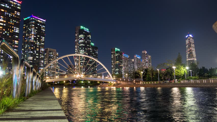 Time lapse of Skyscraper building with bridge illumination on songdo river in central park at Incheon, South Korea