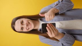 Vertical video of shocked young woman wear shirt use mobile cell phone type swipe chatting send sms doing online shopping order delivery to home, isolated on yellow color background wall in studio - Powered by Shutterstock - Get 15% off with code: PIKWIZARD15
