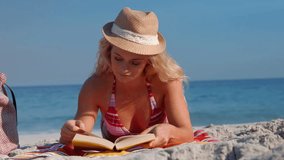 Video of pretty blonde woman lying on towel and reading book
