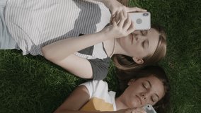 Smiling girls laying on grass using cell phones - vertical video, provo, utah, united states