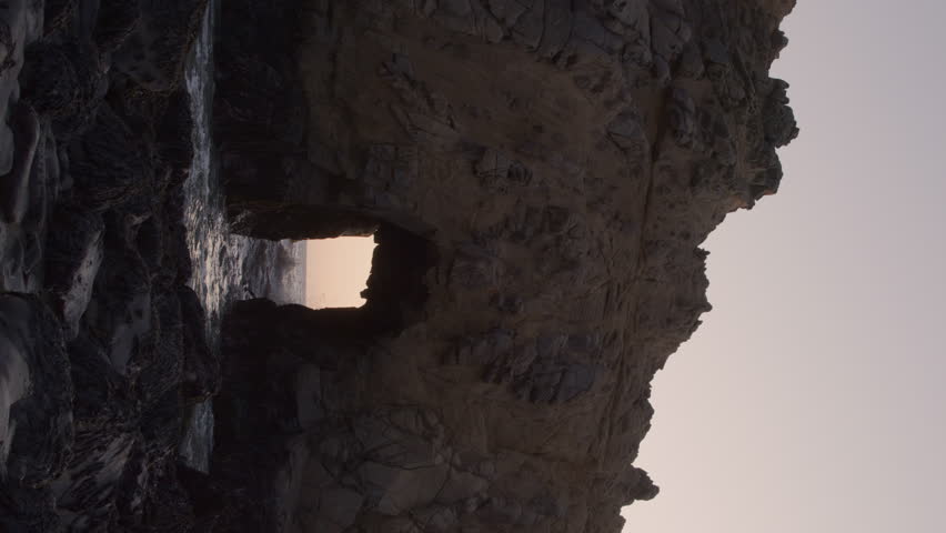 Ocean waves splashing though keyhole arch at sunset - vertical video, big sur, california, united states