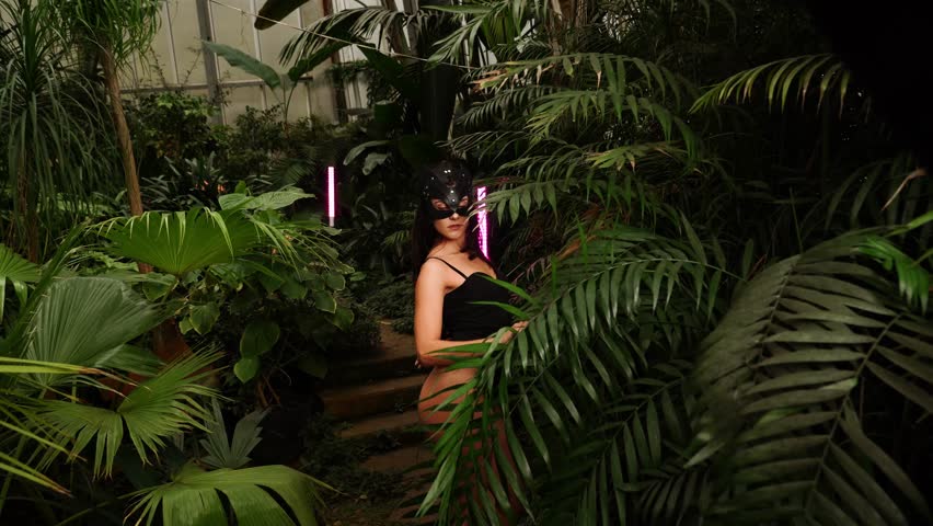 Sexy woman in a BDSM cat mask posing in a tropical garden among palm trees. BDSM concept.4k