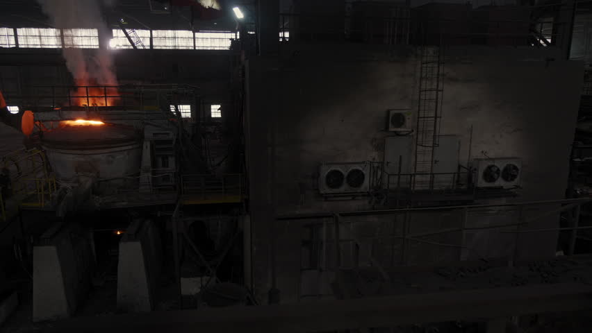 Industrial workshop at the plant. A flame is burning in the furnace. A huge crane transports a vessel with molten scrap metal. Wide shot. Steel plant, Heavy industry. Metallurgy. Slow motion | Shutterstock HD Video #1111586455