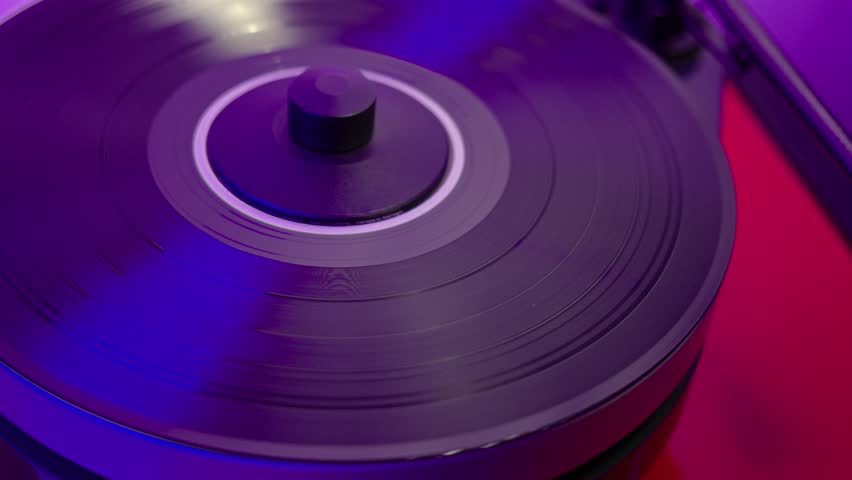 Man's hands turning on high-fidelity vinyl record player, lowering tonearm onto vinyl disc to start listening to music with bluish light in background. | Shutterstock HD Video #1111586787