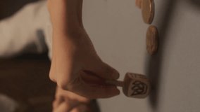 Close-up vertical shot of hand of anonymous Jewish woman spinning wooden dreidel on table at Hanukkah, with visible Hebrew letters Hei - meaning half, and Shin - bet more gelt coin - Powered by Shutterstock - Get 15% off with code: PIKWIZARD15