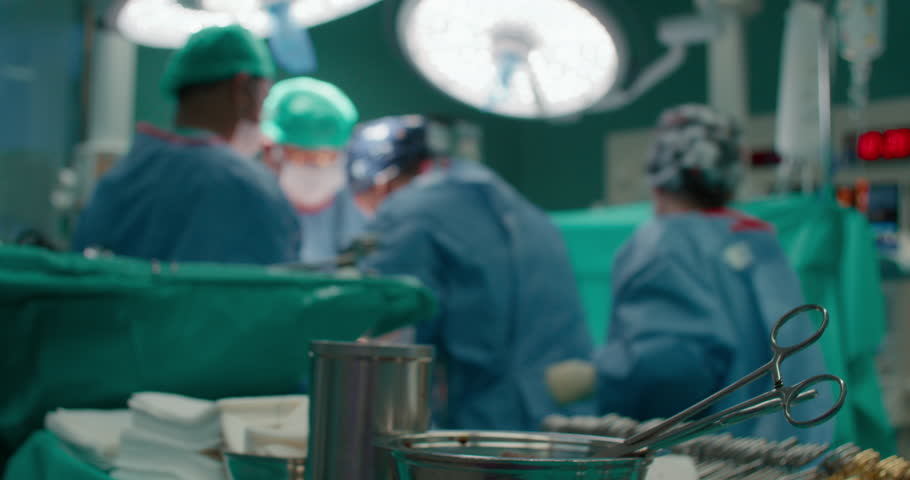 Blurred unrecognizable shot of hospital staff performing surgery in operating room. Surgical instruments on table in operating theatre. Hospital lamp illuminate surgeon and nurses | Shutterstock HD Video #1111589495