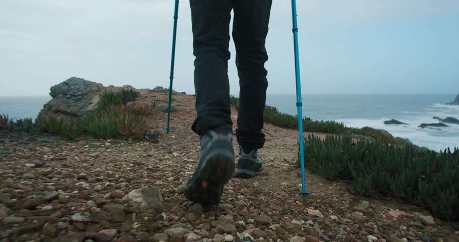 Close up reveal shot, camera follow man walk on path or trail. Lens move from bottom to top, show hiking shoes, jacket, backpack and trekking poles. Young hispanic man in wilderness | Shutterstock HD Video #1111589499