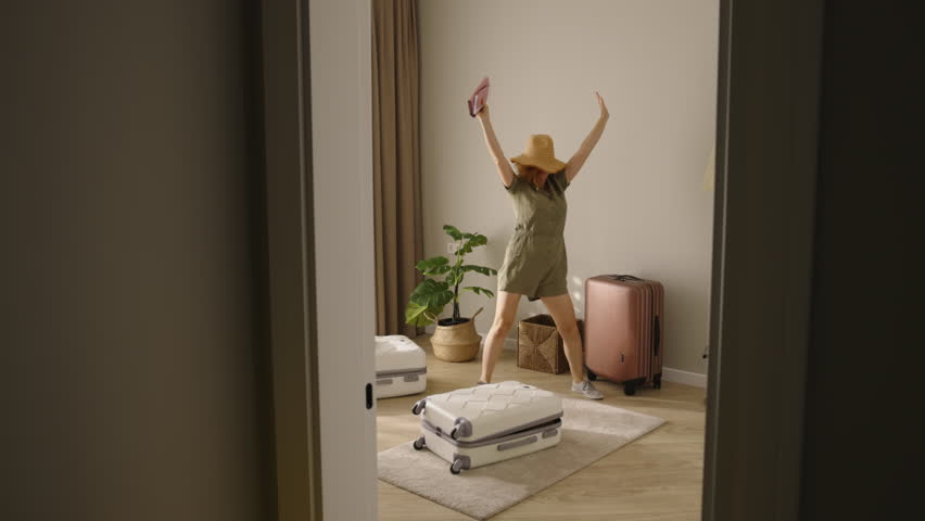 Overflowing with happiness, woman dances packing suitcase. Long-awaited trip is about to come true. Neatly folding clothes, she embraces joy of preparation, after finishing getting ready dances in hat | Shutterstock HD Video #1111591687