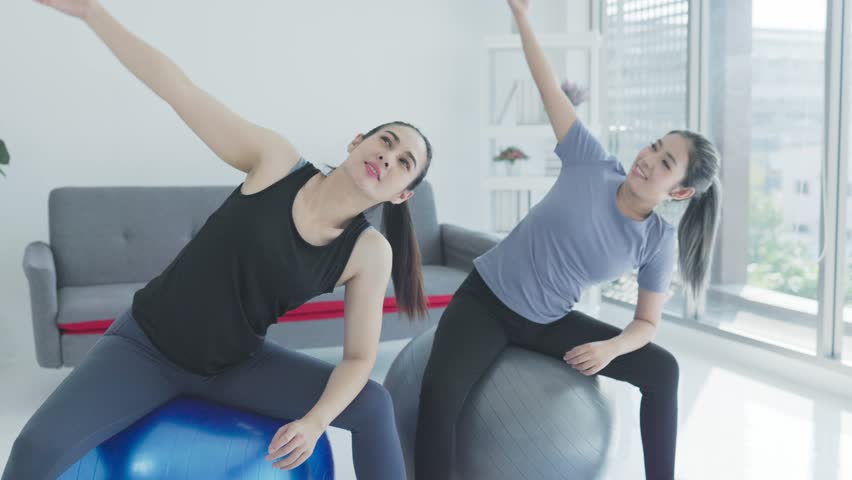 Young asian women with exercise trainer stretching her arms sitting on balls | Shutterstock HD Video #1111593847
