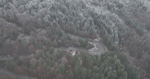 Aerial view of mountain twisted road in the winter and driving car. Epic, snowy white winter and snow capped forest. Road through frozen forest, 4k video.
