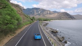 Aerial view blue convertible car driving by coastal road along dramatic rocky shore towards volcanic mountains on Oahu island. Happy young couple traveling by Hawaii. Summer vacation adventure tourism - Powered by Shutterstock - Get 15% off with code: PIKWIZARD15