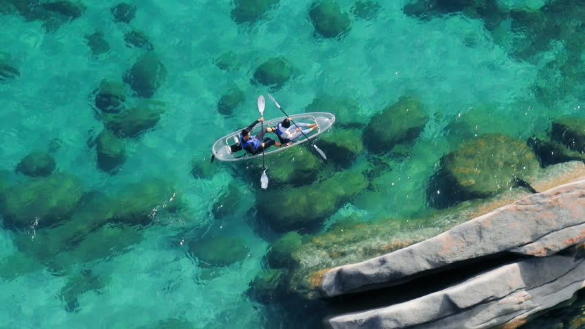 Aerial view couple kayaking together in pristine blue lagoon in lake Tahoe. Tourists on weekend adventure paddling in clear kayak. Water sport activity leisure. Sunny light refracting on clear water