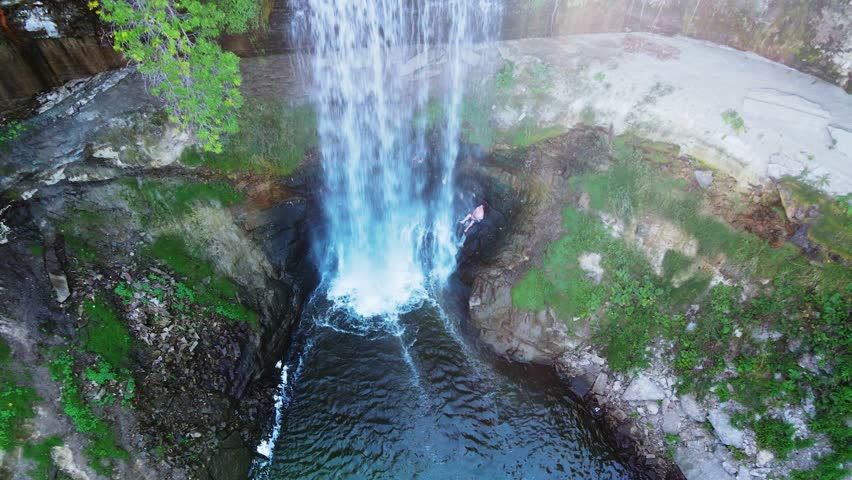 Aerial Drone View of Minnehaha Waterfall, Minnesota. The video beautifully captures the waterfall surrounded by lush greenery, with water cascading down the rocks in a stunning display. 