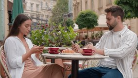 Caucasian couple in city cafe using mobile phone telephone texting working serious man woman breakfast outside together gen z drinking coffee chatting businessman businesswoman separation concentrated - Powered by Shutterstock - Get 15% off with code: PIKWIZARD15