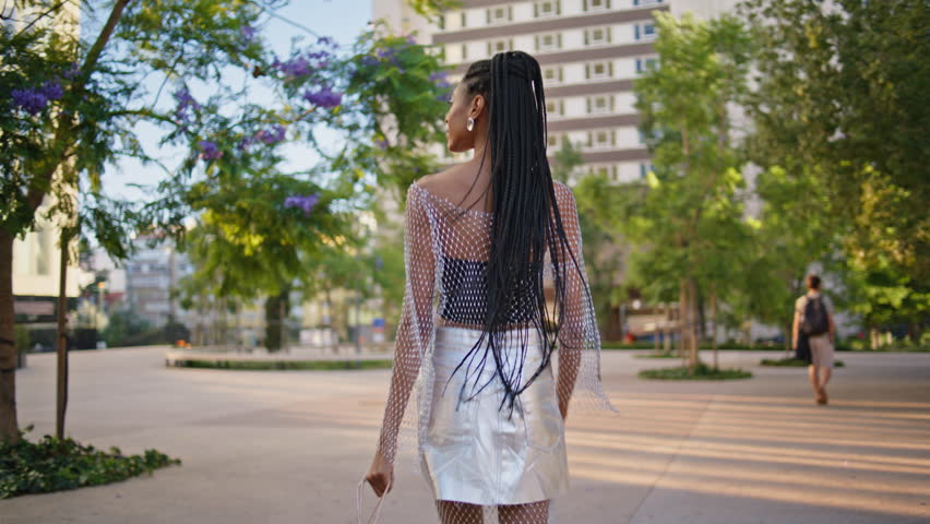 Relaxed brunette walking city back view. Tourist african american girl enjoying summer stroll looking asides at downtown. Stylish fashionista with afro braids hairstyle stepping square on high hills | Shutterstock HD Video #1111603663