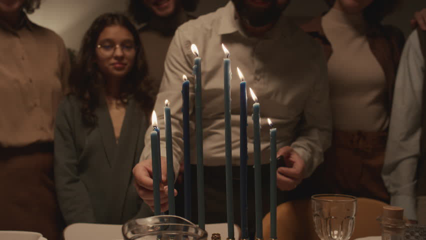 Medium shot of middle-aged Jewish man in kippah skullcap lighting up eight Hanukkah candles on menorah using shammash, then putting it in middle, singing and dancing with joy Royalty-Free Stock Footage #1111606863