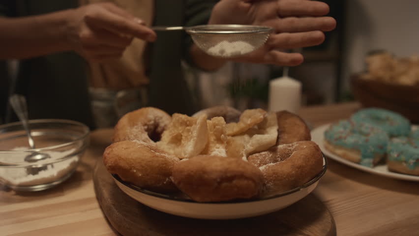 Close-up shot of hands of anonymous young girl dusting doughnuts and fritters on dish with sugar powder using sieve, while preparing for family celebration Royalty-Free Stock Footage #1111609587
