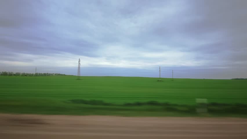 Meadows fields, electric power transmission towers on background. Cloudy weather, overcast. Traffic barrier guard rail along highway. View through side window of van in motion. Roadway out of town Royalty-Free Stock Footage #1111615601