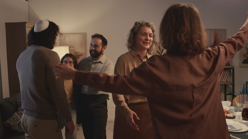 Medium shot of Jewish woman greeting and hugging female friend arriving for Hanukkah celebration, while husband in kippah and daughter standing and chatting to male relative Royalty-Free Stock Footage #1111618087