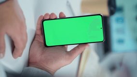 Close-up Of Mobile Phone With Green Mock-up Screen In Men's Hands On Desktop Background. Man Using Smartphone, Browsing Internet, Social Networks, Financial Reports.