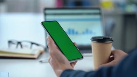 Close-up Of Mobile Phone With Green Mock-up Screen In Men's Hands On Desktop Background. Man Drinks Coffee and Uses Smartphone.