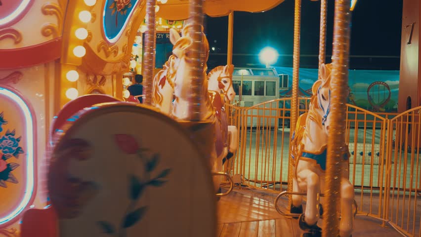 A carousel or carrousel, merry-go-round, roundabout, or hurdy-gurdy is amusement ride consisting of a rotating circular platform with horse seat for riders. Colorful flashing light of vintage carnival Royalty-Free Stock Footage #1111619357