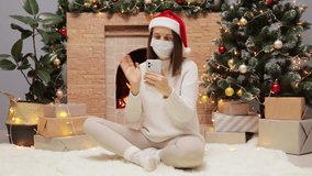 Sick Caucasian woman wearing face mask and Sant Claus hat using smartphone for video call with family or friend at home during Christmas holiday prevent from covid new variant omicron. - Powered by Shutterstock - Get 15% off with code: PIKWIZARD15
