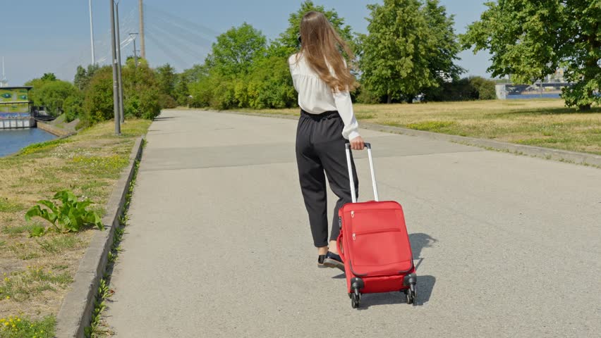Female tourist walking with red suitcase over empty road along river, Riga