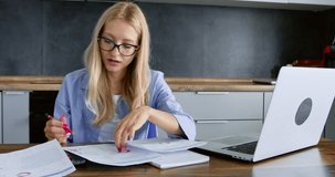 Young woman looks through accounting paper documents at home workplace. Blonde lady freelancer in glasses advises with colleague on phone