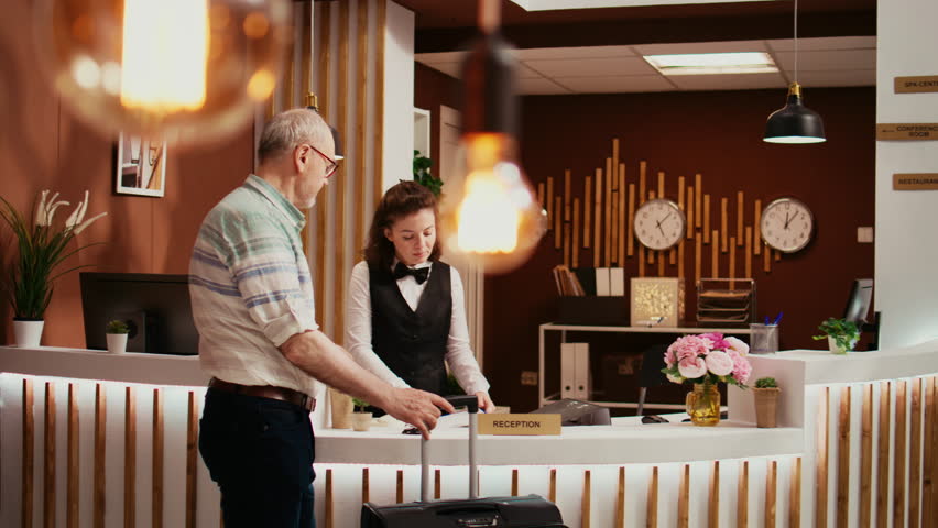 Elderly tourist signing check in papers at front desk, going through registration formalities with hotel staff at holiday retreat. Traveller registering at all inclusive resort, hospitality industry.