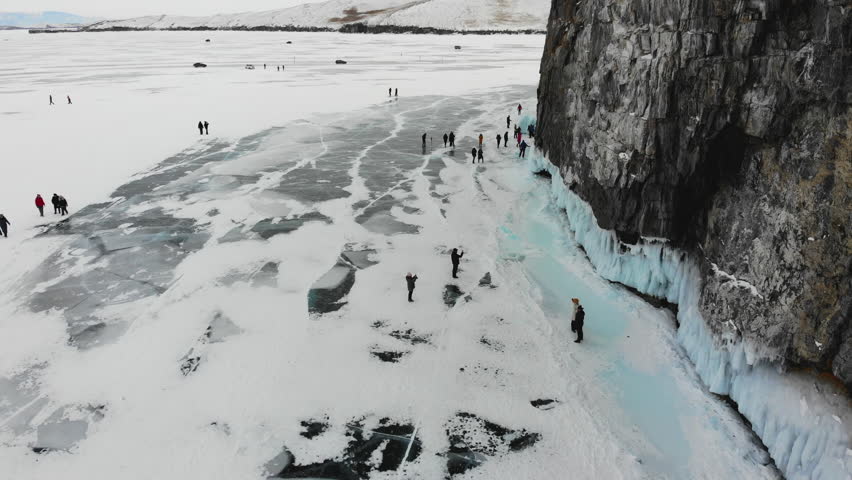 Tourists walk on the ice of the frozen Lake Baikal, admire icicles on the rocks. Winter trip.