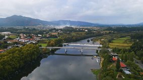Stunning aerial 4K drone footage of a village - Ponte de Lima in Portugal and its iconic landmark - Stone roman bridge crossing over the Lima River. Filmed in autumn during partly cloudy weather.