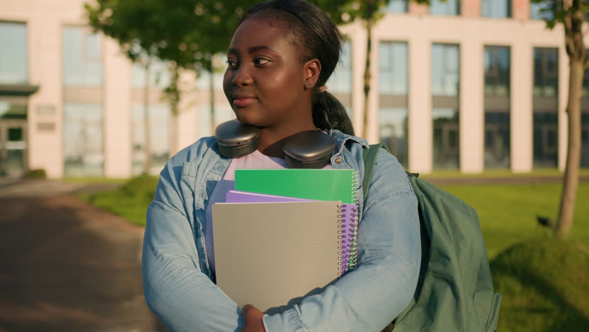 African American woman university college student teen girl high school pupil lady holding copybooks books with schoolbag headphones posing in city outdoors smiling at camera study education studying Royalty-Free Stock Footage #1111629317