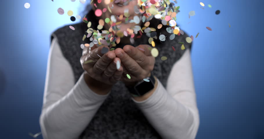 Person blowing confetti toward camera in super slow-motion captured with a high speed camera at 800 fps and blue backdrop. Anniversary birthday celebration concept Royalty-Free Stock Footage #1111633149