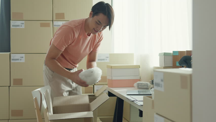 Candid of youth attractive Asia male entrepreneur E-commerce small business prepare product put in cardboard box check detail sale purchase order from laptop computer at small online retail shop. | Shutterstock HD Video #1111634869