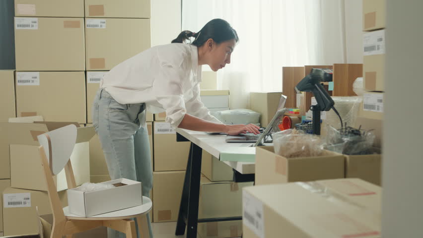 Youth attractive Asia female entrepreneur small business check parcel box key barcode number on cardboard box in laptop computer check inventory product ready for shipment at small online retail shop. | Shutterstock HD Video #1111634901