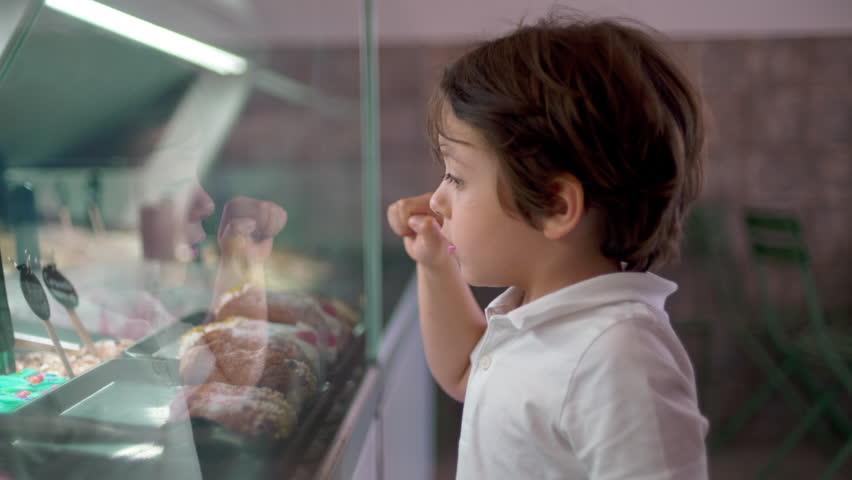 One small boy pointing at ice-cream flavor behind glass counter. Child picking dessert taste with finger