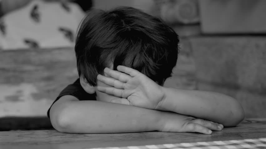 Depressed child hiding face with arms struggles with anxiety and loneliness. Isolated kid covering himself in shame in dramatic monochromatic, black and white Royalty-Free Stock Footage #1111638015