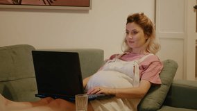Future mom to be touches her tummy while using laptop on the couch. Cheerful pregnant laying on sofa looking at laptop screen, watching funny movies or chatting on internet with friends. - Powered by Shutterstock - Get 15% off with code: PIKWIZARD15