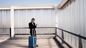 Young Caucasian woman stands with blue suitcase at an airport, immersed in smartphone app, coordinating next flight or arranging meeting, embodying blend of modern travel and business communication. - Powered by Shutterstock - Get 15% off with code: PIKWIZARD15